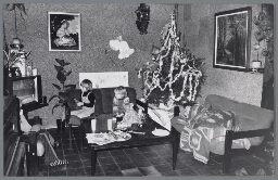 Een gezin zit in een met kerstboom versierde huiskamer naar de televisie te kijken. 1978