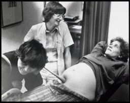 Lin Pugh, partner van de zwangere Moniek van der Kroef, luistert naar het hartje van de baby, in aanwezigheid van gynaecologe Helen Brandenburg 1982