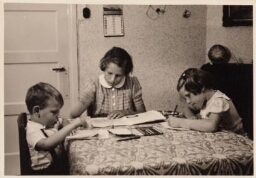 Kiekje van twee zusjes en broertje die aan tafel huiswerk maken en tekenen. 195?