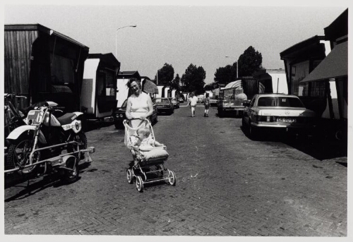 Een vrouw poseert met een kind in een kinderwagen in een woonwagenkamp. 1987