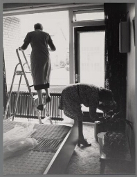 Alphahulp aan het ramen zemen bij een bejaarde dame. 1982