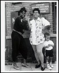 Twee zwarte vrouwen en een kleine jongen staan voor de ingang van  Stichting Vrouwen Vakschool voor Informatica 198?