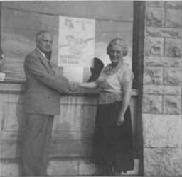 Mies Boissevain-van Lennep, activiste, schudt de hand van een man staand voor een affiche met propaganda in 1949, Pembroke tijdens haar reis in Amerika. 1949