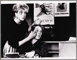 Vrouwen schminken elkaar 'een blauw oog', op de achtergrond hangt het affiche van de Stichting Tegen Haar Wil. 198?