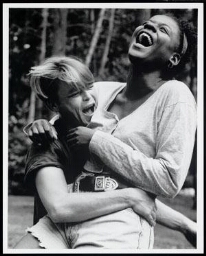 Witte vrouw heft lachende zwarte vrouw op schoot 1995