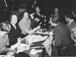 Leden zitten aan tafel tijdens de 4e Algemene jaarvergadering? Op de achtergrond speelt een muziekbandje. 1937