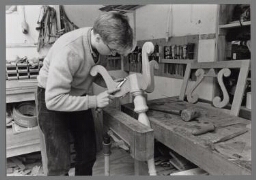 Meubelmaakster bewerkt hout op een werkbank. 1985