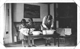 Twee meisjes en een onderwijzeres van een Montessorischool wassen samen af in een klaslokaal. 191?