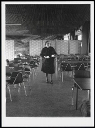 Vrouw met twee kop en schotels in haar hand in een lege kantine 1986