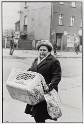 Vrouw lopend over straat met boodschappentas en wasmand. 1982