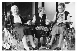 Zuster Lydia met twee bejaarden vrouwen in een rolstoel. 198?