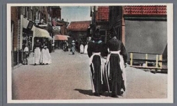 Vrouwen in klederdracht lopen over straat. 1900?