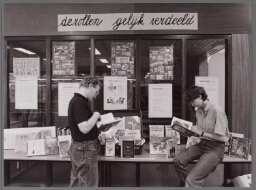 Een man en een vrouw bekijken uitstalling van kinderboeken onder het thema 'de rollen gelijk verdeeld'. 198?