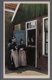 Drie vrouwen in Volendamse klederdracht staan voor een huis, twee vrouwen staan in de  deuropening 1900?