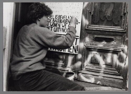 Een vrouw schrijft een manifest, opgehangen bij de deur van het kraakpand van de vrouwenwoongroep. 1983