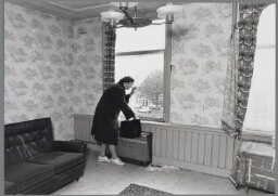 Een vrouw staat in een bijna uitgewoonde kamer bij het raam en wacht 1988