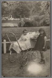 Meisje staat naast kind in kinderwagen in het park. 190?