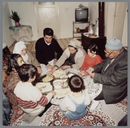 Turks gezin tijdens een gezamenlijke maaltijd, ze zitten op de grond in de kamer 2000