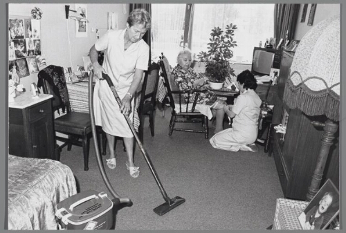 Verzorgster en schoonmaakster aan het werk in een bejaardentehuis. 1988