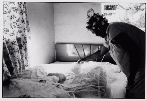 Moeder staat bij een groot bed met pasgeboren baby erin. 1986