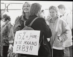 Bijstandsvrouwen in een tent op Vredenburg in Utrecht met een affiche op een rugtas: '15% + f 400,- in de maand erbij!!'. 1989