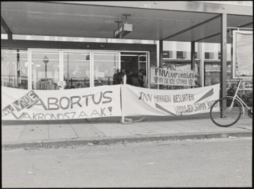 Vrouwen voeren actie tijdens het FNV fusie congres, voor de ingang van het gebouw spandoeken met tekst: 'Vrije abortus Vakbondszaak', 'FNV mannen besluiten vrouwen staan buiten'. 1981