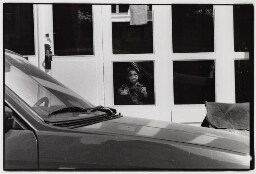 Een jongetje kijkt uit het raam van een commercieel kinderdagverblijf. 1989