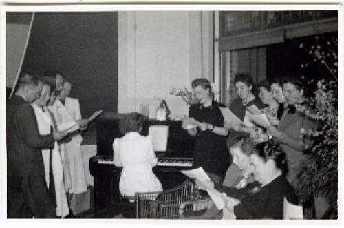 Grietje Brink staand naast de piano (6e van links) zingend met Johanna Westerdijk (zittend 3e van links) en andere collega's van het Phytopathologisch Laboratorium 'Willie Commelin Scholten' (WCS) in villa Java 1948