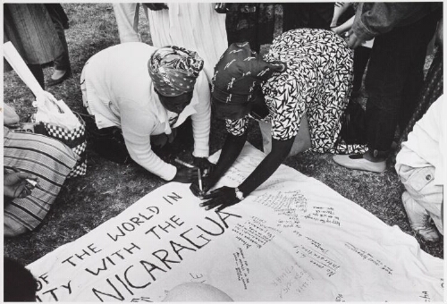 Een aantal zwarte vrouwen schrijven protest teksten op een groot laken tegen oorlog en voor mensenrechten tijdens de wereldvrouwenconferentie. 1985
