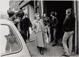 Twee vrouwen lopen tussen twee rijen jongens door. 1982