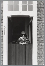 Oudere vrouw staand bij haar deur. 1987