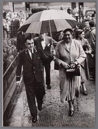 Bijschrift: 'Queen Salote of Tonga (the Friendly Isles) arrives ath the Royal George Hotel, Perth, June 19, under the shelter of an ubrella held by head porter Kenneth MacLean, of Ross-Shire 195?