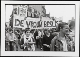 Groep vrouwen loopt in demonstratie  Voorop een spandoek met tekst 'De vrouw beslist'. 1980