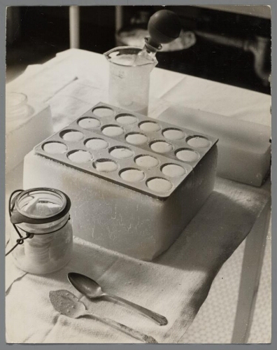 Flessen met schijfjes bevroren moedermelk en het ijsblok waarop de schijfjes bevroren worden. 1937