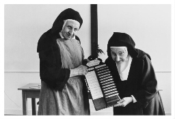 Twee Carmelitessen met 'de lijst der bedieningen', het rooster, van zondag. 1982