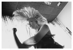 Meidengroep doet popmodeshow.Een van de meiden showt een enorme 'hanekam', haar lange haar staat als een waaier recht op haar hoofd. 1990