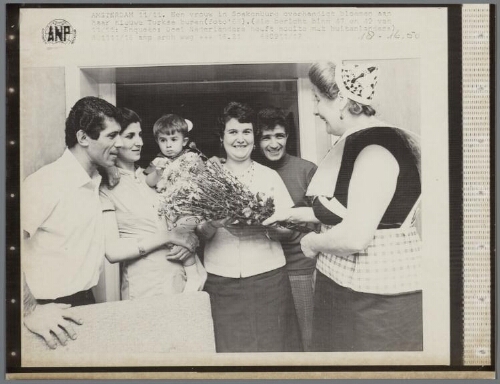 Een vrouw in Spakenburgse klederdracht overhandigt bloemen aan haar nieuwe Turkse buren. 1968