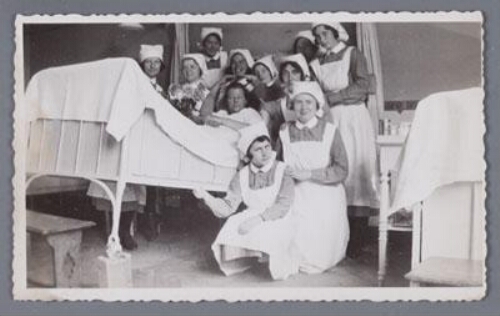 Verpleegkundigen in uniform poseren bij een patiënt in bed. 1931