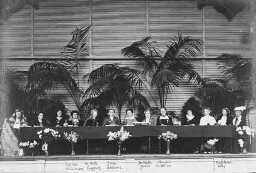 Congreszaal met 13 deelneemsters aan een lange tafel op een podium aan het 'International Congress of Women', oftewel het 'Internationaal Congres van Vrouwen', gehouden van 28 april - 1 mei 1915 in de congreszaal van de Haagse Dierentuin (ook wel Moors Paleis genoemd), gelegen naast het Malieveld, in Den Haag, Nederland 1915
