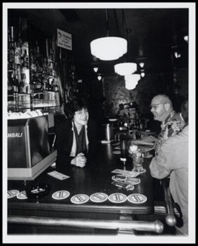 Portret van Mieke Martelhof (1947), eigenares van café Vivelavie in Amsterdam, aan de praat met klanten in haar café 1998