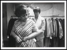 Vrouw past jurk in winkel met hulp van de verkoopster 1986
